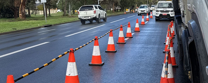 Traffic management setup with orange and white cones marking a construction zone on a wet road, illustrating advanced traffic control measures for TC2 / TMI2 training.