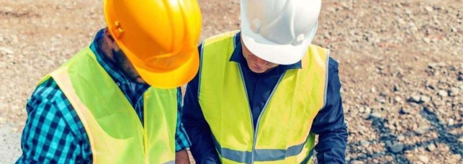 Two construction workers in safety vests and hard hats reviewing plans on a job site, emphasizing workplace safety and traffic management training.
