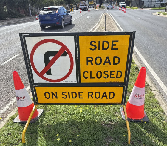 Road sign indicating "Side Road Closed" with no right turn symbol, surrounded by traffic cones, emphasizing safety in traffic management training context.